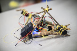 Stickbot, a small robot composed of sticks, circuitry, actuators, a microcontroller, and a motor driver, lashed together with string.