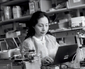 Black and white photo of Jenny Jiang working in her lab on a laptop.